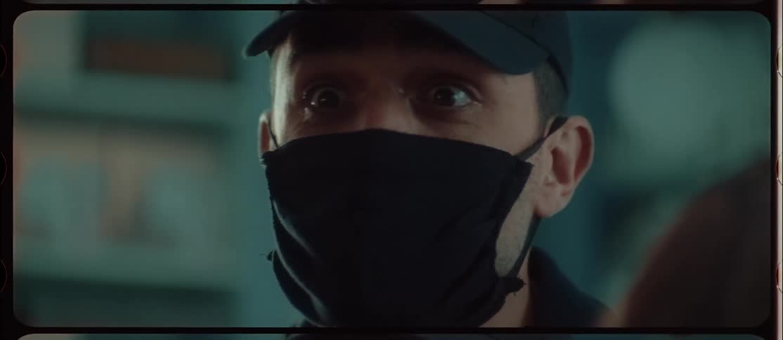 A man standing outside talking gestures with his hand in front of his face mask and shakes his head