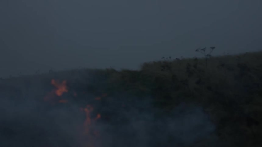 A fire smokes and burns in an open field