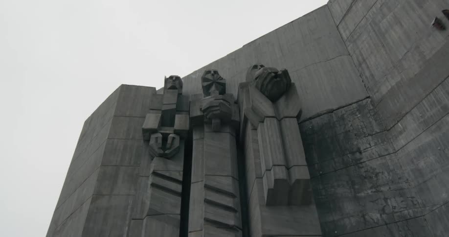 A concrete building with sculptures with the sky and clouds in the background