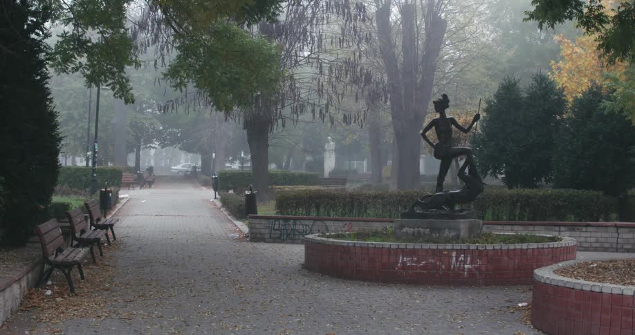 Mist covers park near plaza with statue sitting in large planter