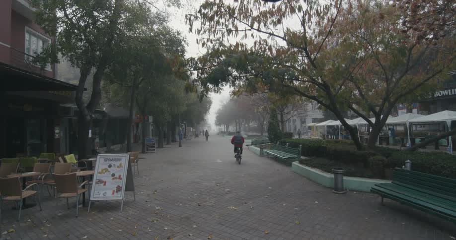 A person bikes down a street lined with shops and passes by a pedestrian walking