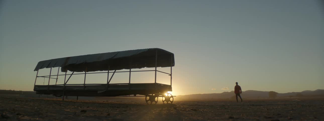 A man walks past an empty feed trailer in a barren paddocl