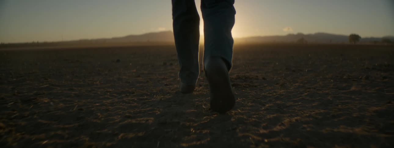 A man is walking through a dirt flatland in the wilderness at dawn