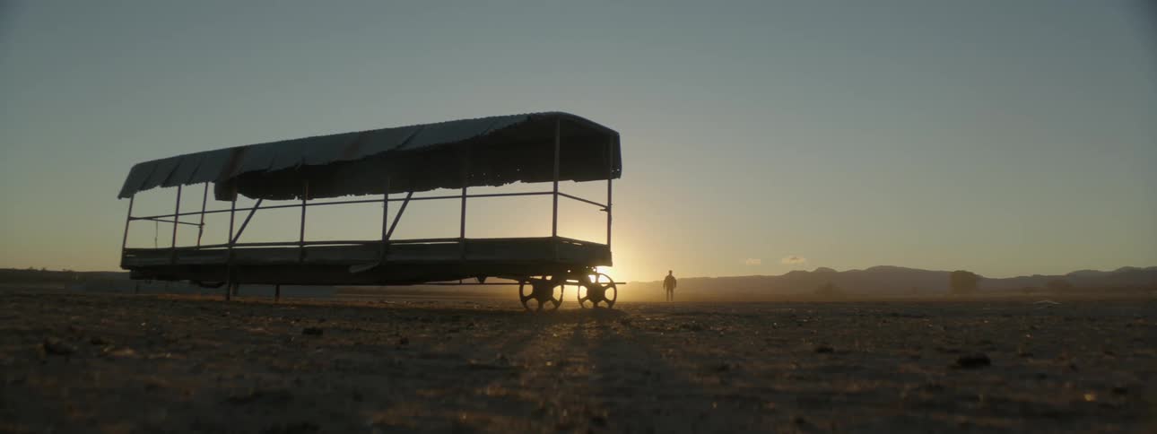 A man walks behind a large feed wagon in a barren paddock
