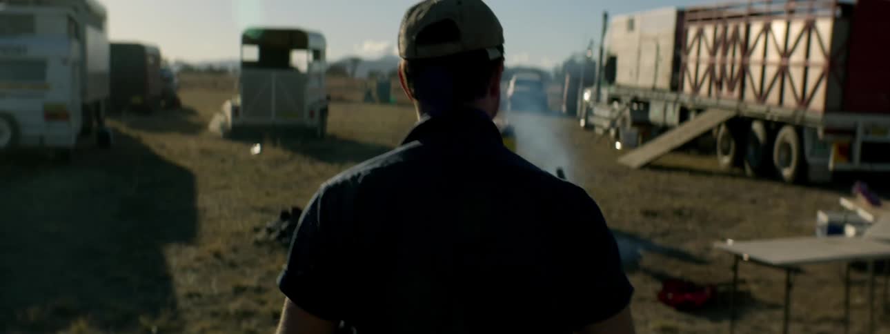 A man is walking through a dirt lot full of trucks trailers and livestock