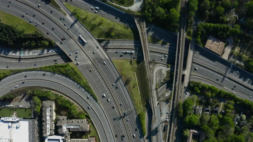 Traffic flows along highways bordered by buildings and vegetation