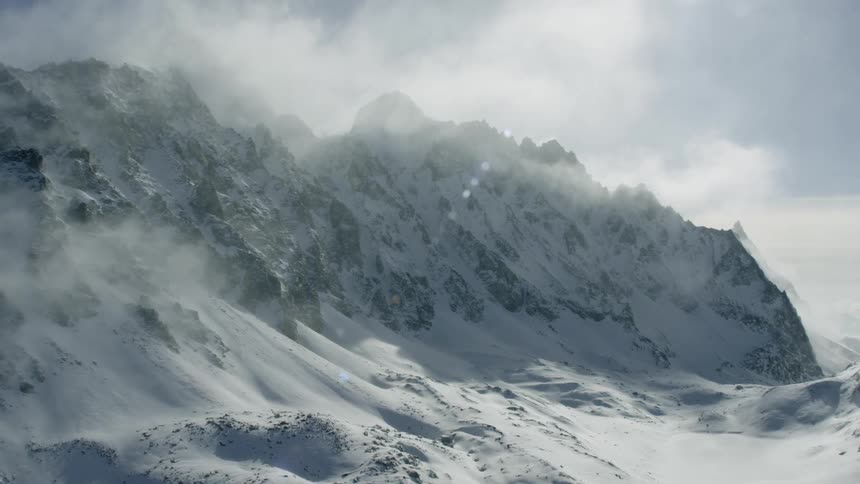 Clouds are drifting over snow-covered mountains during the day