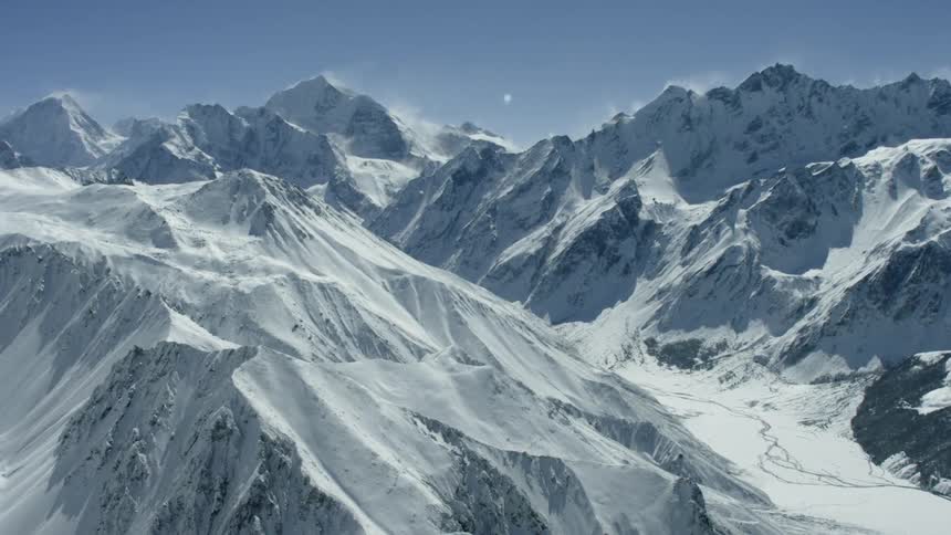 Snow is drifting off of mountain peaks on a sunny day