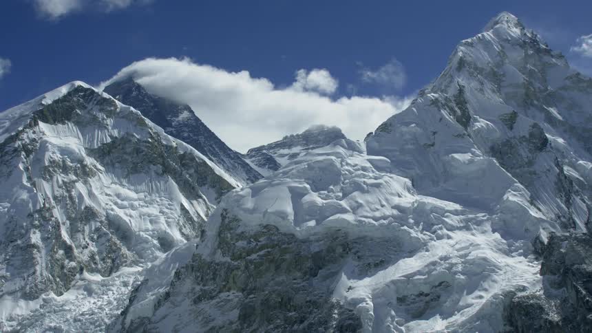 Clouds are drifting over snow-covered mountains during the day
