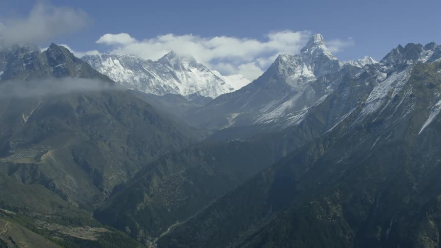Clouds are drifting over snow-covered mountains during the day