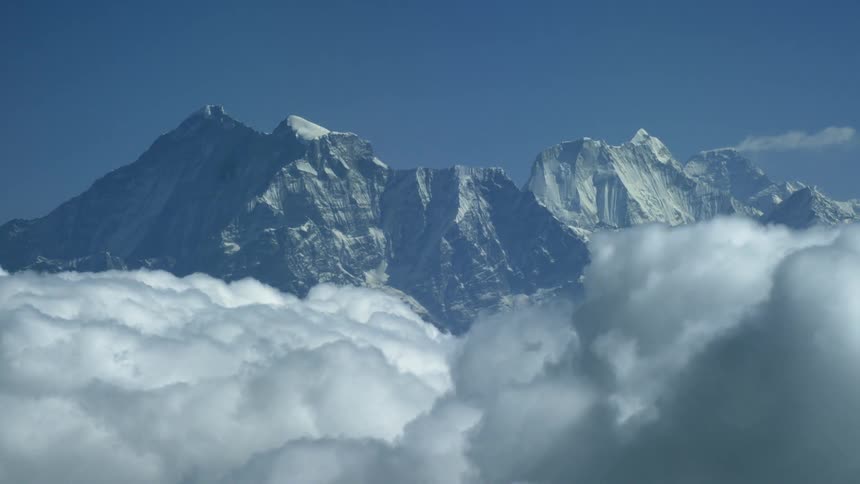 Clouds hang above and pass through a tall mountain