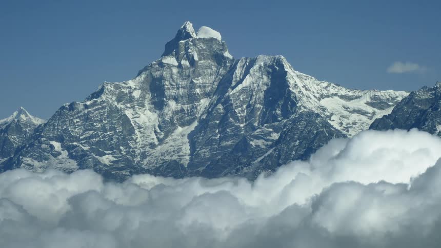 A tall snow covered mountain pierces through the clouds