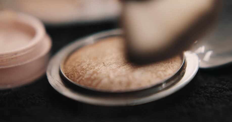 A makeup brush taps the bronze colored powder in a small compact