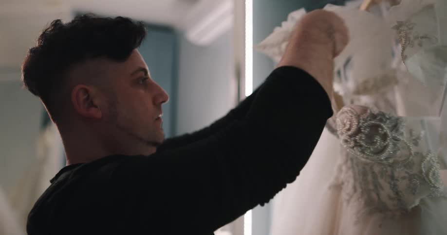A man in a room taking a dress from a rack with a wall and mirror in the background