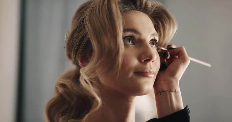 Makeup artist with tattoo on wrist applies makeup to woman
