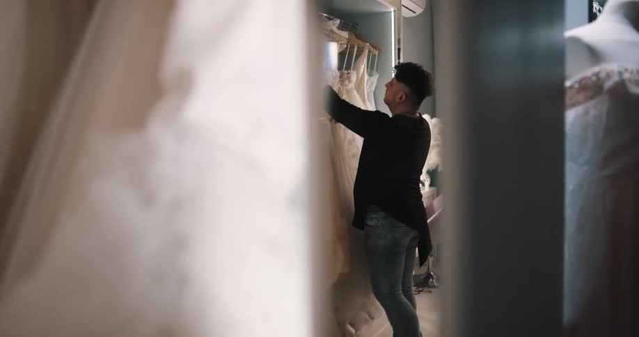 A male employee is searching for and selecting a wedding gown from a closet during the day
