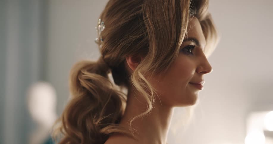 A woman has her makeup done and hair curled and styled in a ponytail