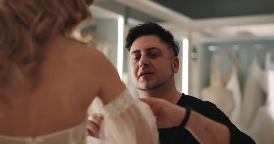 Wedding shop worker helps bride try on wedding dress