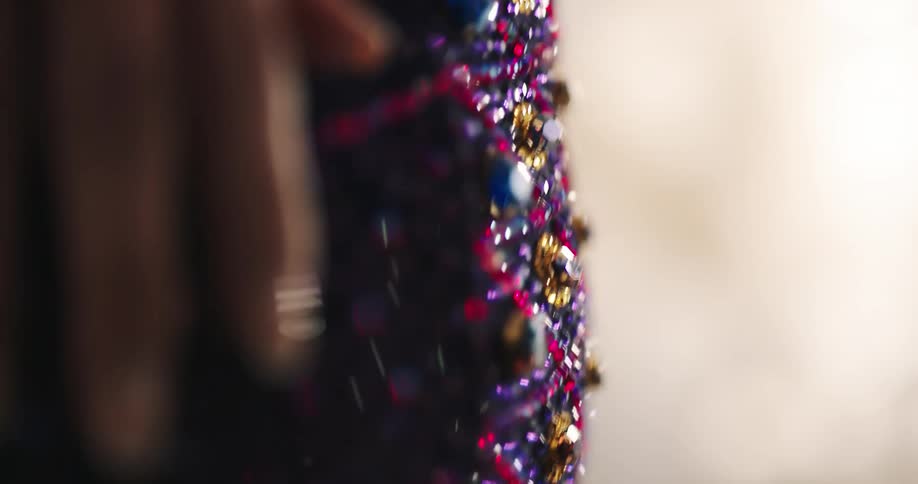 Woman wearing a colorful sequin dress rubs her hand over the sequins