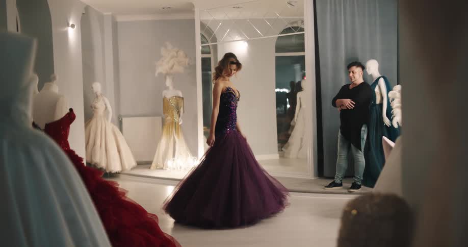 Dress shop attendant watches as customer sways back and forth checking fit of evening gown