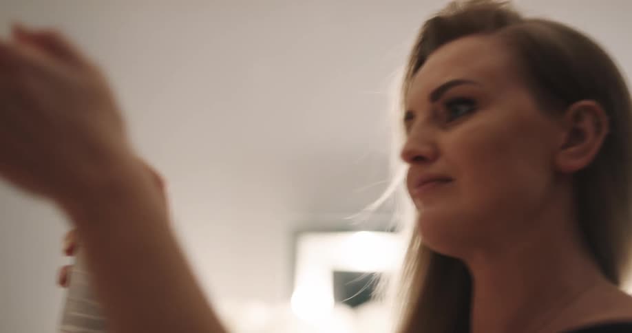 Blonde female hairdresser sprays brown wavy hair of woman in salon