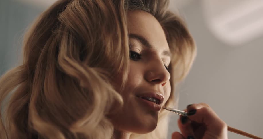 Person wearing fingernail polish applies lipstick to woman using brush