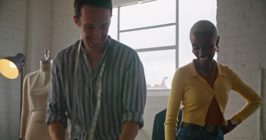 A black woman wearing a yellow sweater is talking to a man with a tape measure around his neck