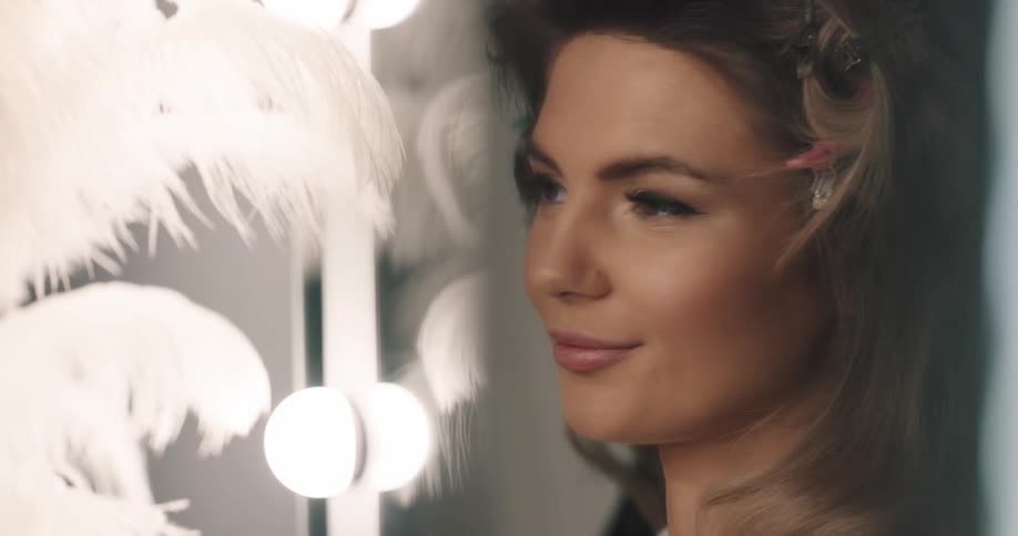 A woman smiles at her reflection in the mirror after a makeup artist applies blush