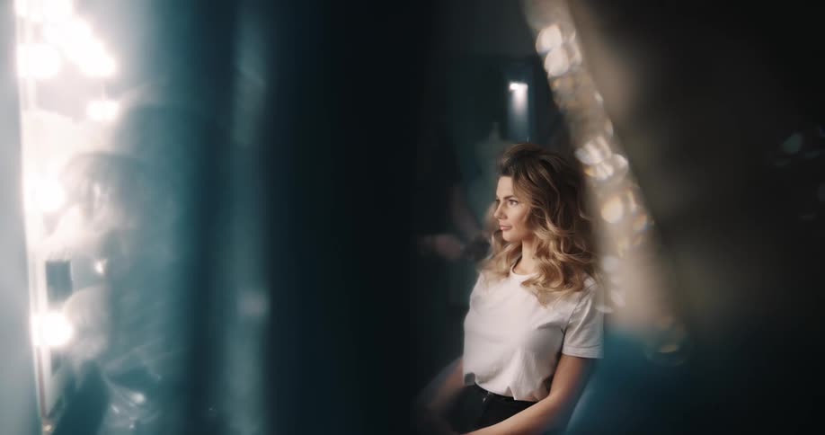A woman in a room sitting as another woman does her hair with a mannequin and a wall in the background