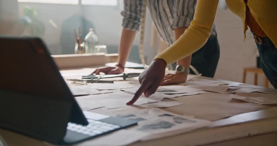 A fashion designer calls her colleague over to look at a design on a laptop