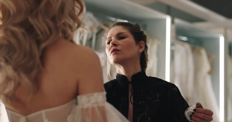 A woman in a bridal store is putting makeup on a woman wearing a wedding dress