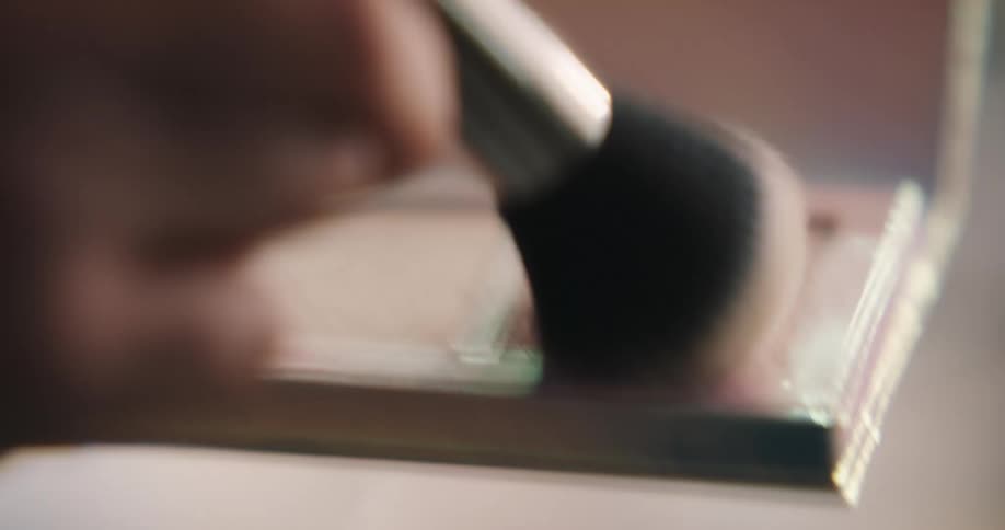 A woman uses a blush brush to pick up bronzer and highlighter in a compact