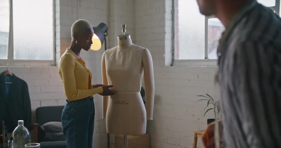 Male and female designer discuss making dress on mannequin with each other in workshop