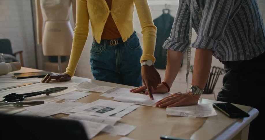 Man and woman stand in design studio around table with papers and patterns holding discussion