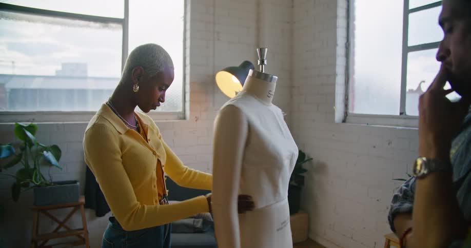Male and female designer discuss making dress on mannequin with each other in workshop