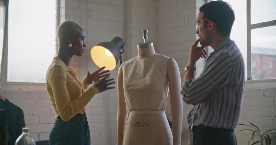 A woman speaks to a man as they stand together around a mannequin