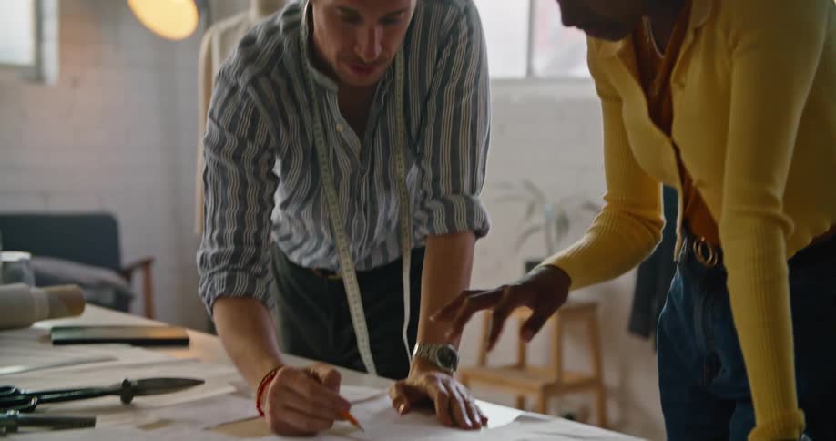Two clothing designers are talking and looking at drawings on a table
