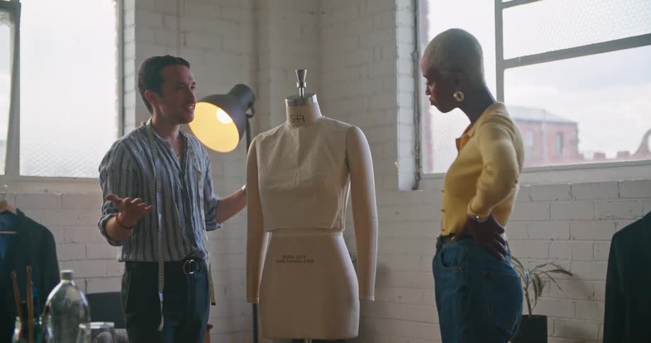 Male and female designer discuss making dress on mannequin with each other in workshop