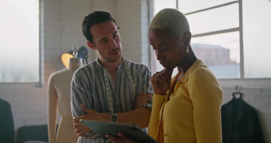 A man and a woman in a room with a mannequin looking at a tablet with a wall and window in the background