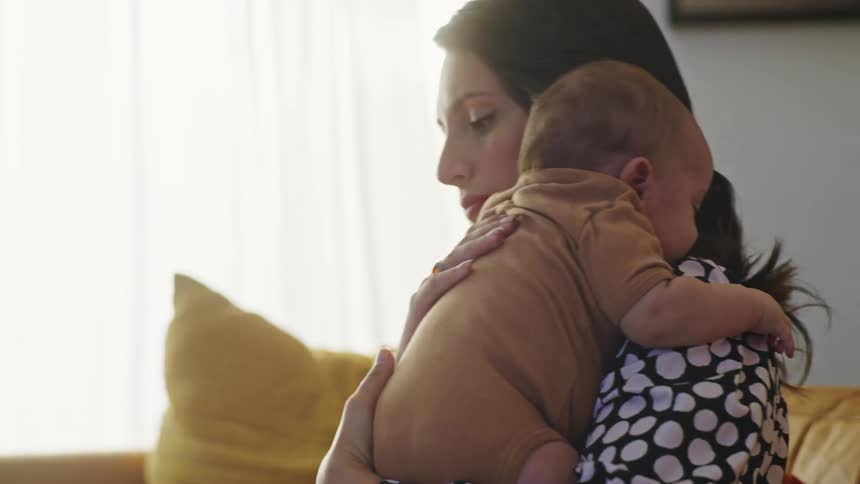 A woman is sitting on a sofa in a home while lifting and holding a baby