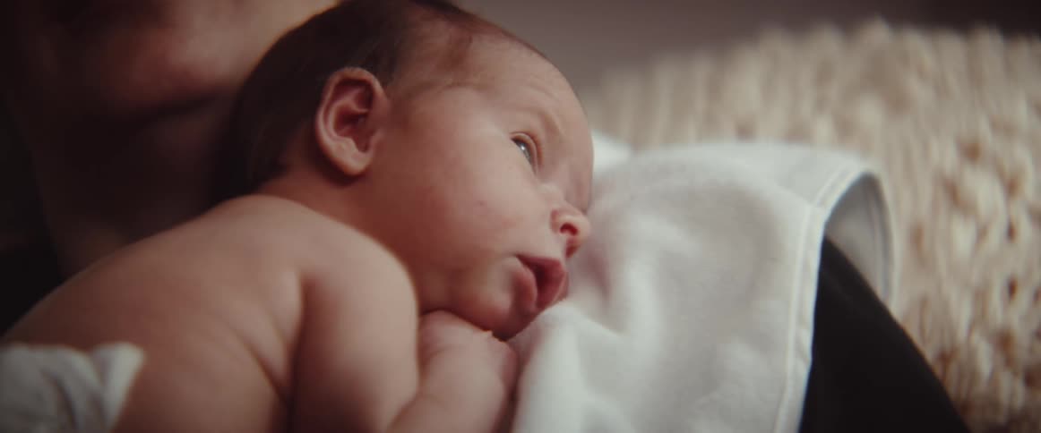A man is resting an infant on a towel on his shoulder