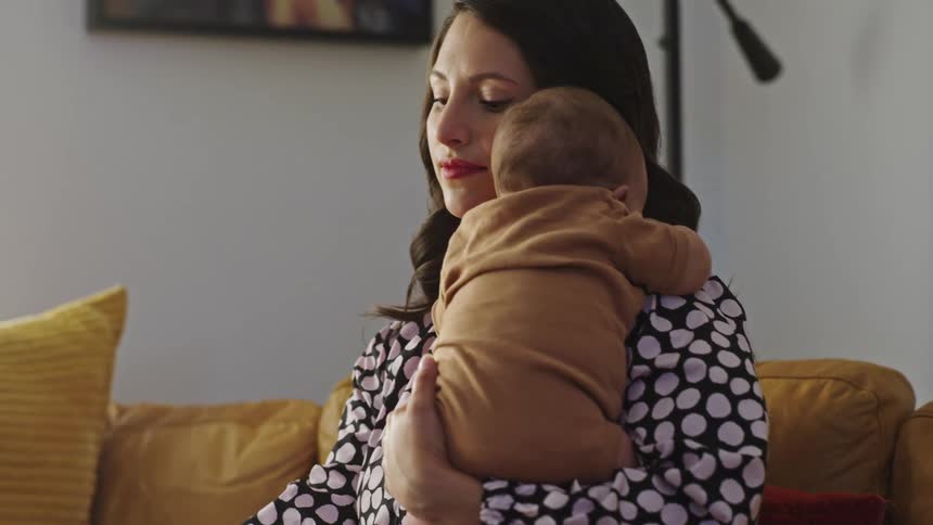 A mother holding her baby sitting on the couch