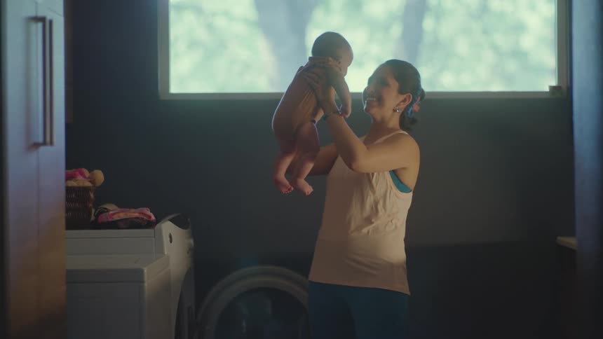 Mom holds baby up smiling and making faces while standing in laundry room