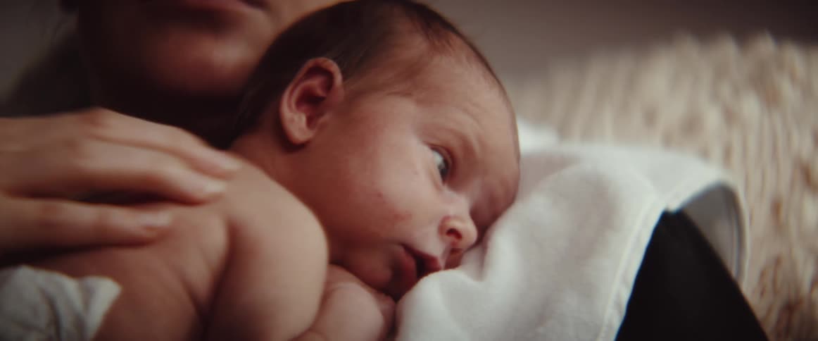 A woman kisses and rubs the back of an infant while sitting indoors