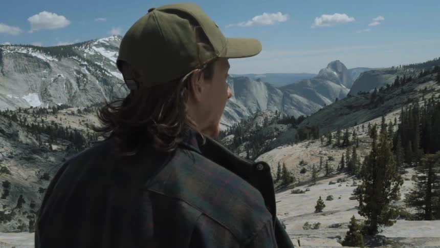 A man looks out over a mountain range on a windy day