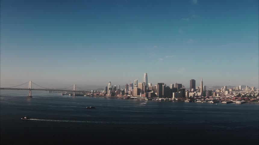 A ferry and a sailboat move through the ocean and toward downtown