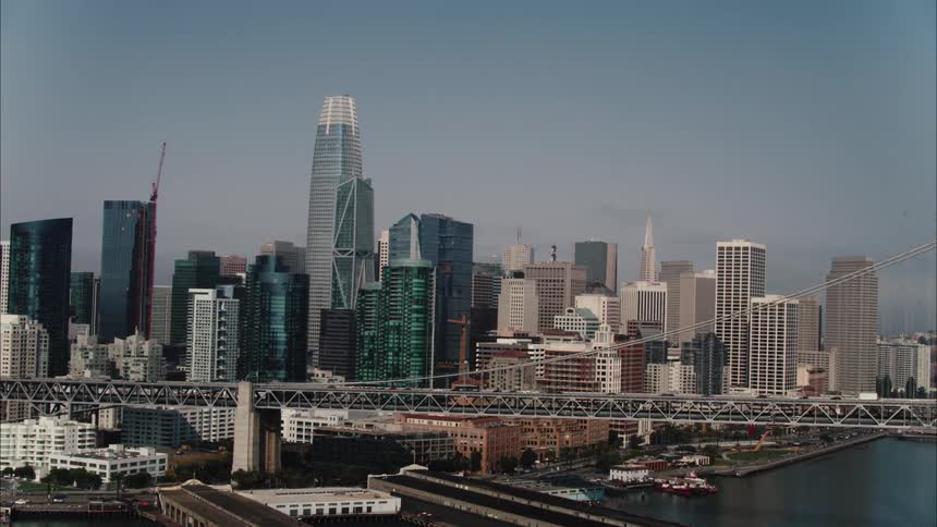 A city skyline with buildings and skyscrapers with a bridge in the foreground and the sky and clouds in the background