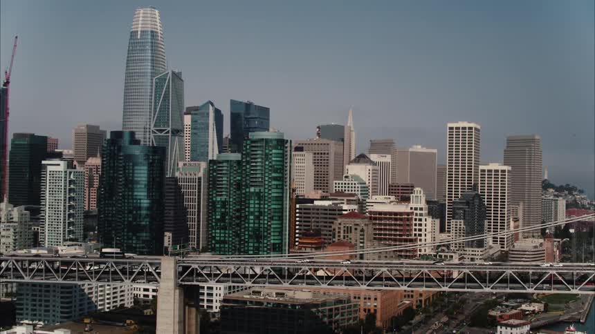 Traffic flows across suspension bridge over water passing city downtown
