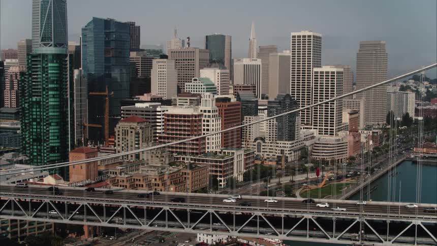 Traffic moves across a bridge going into a city with tall modern buildings along the skyline