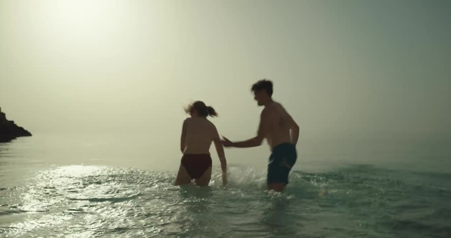 A couple run into the water of the beach